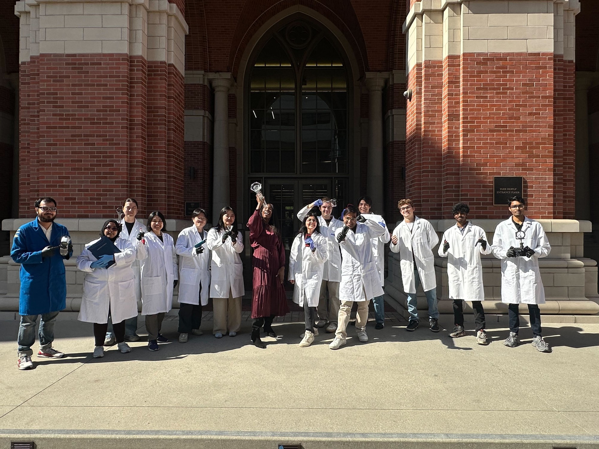 The Sustainable Lab team in lab coats, smiling and holding research equipment outside a USC campus building